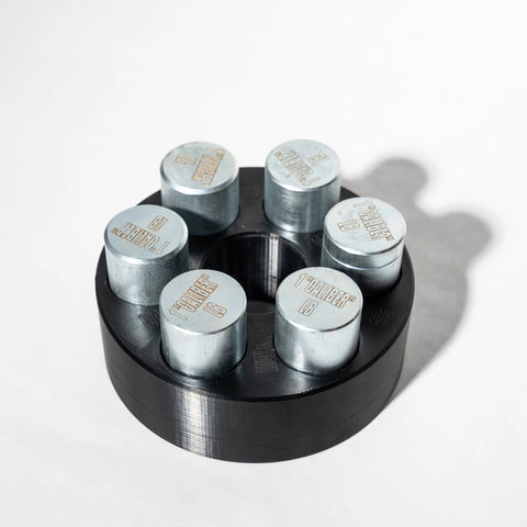 A black circular base holds six evenly spaced silver cylinders, engraved “1 CHAMBER 18,” resembling a revolver. These are Weight It Out Lock and Load Revolver Micro Loading Plates—perfect for a customizable workout. White background.