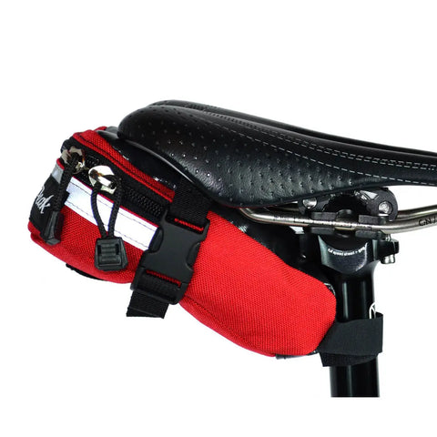 Close-up of a black bicycle seat with a Lone Peak Packs Tool Pouch Seat Bag in red and white attached underneath, secured by black straps and buckles—a practical accessory for carrying riding essentials.