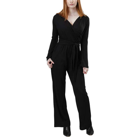 A woman with straight red hair wears the Spiritex Long Sleeve Surplice Jumpsuit in Organic Cotton/Tencel and black shoes, posing confidently with one hand in her pocket against a white background.