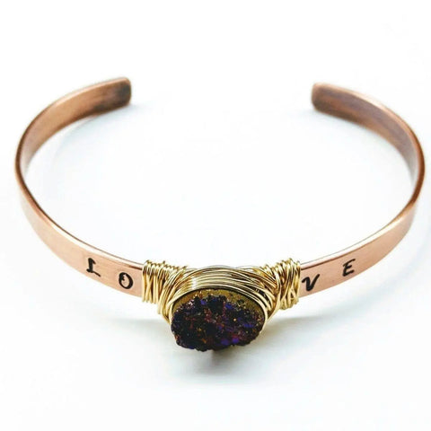 The LOVE Stamped Gold Wire Wrapped Purple Druzy Copper Cuff by Alexa Martha Designs features a handmade copper band with LOVE stamping and a central cluster of glittery purple druzies wrapped in gold wire.