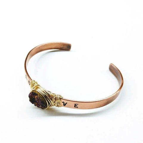The LOVE Stamped Gold Wire Wrapped Purple Druzy Copper Cuff by Alexa Martha Designs is a handmade, minimalist copper bracelet engraved with LOVE and featuring a rough purple druzy agate crystal wrapped in gold wire.