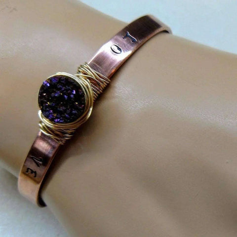 The LOVE Stamped Gold Wire Wrapped Purple Druzy Copper Cuff by Alexa Martha Designs showcases a round purple druzy on a copper band with gold wire wrap and engraved LOVE symbols.