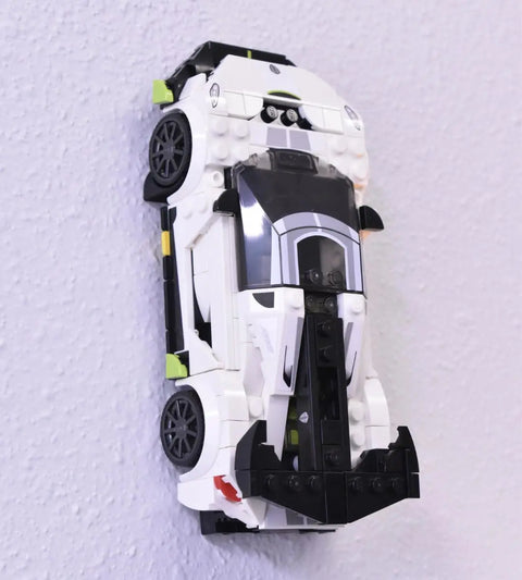 A white and black LEGO race car model is mounted vertically, front bumper down, on a light purple wall using the Chatelet Manufacturing Low Profile Collectible Car Display Wall Mount (White), compatible with LEGO cars.
