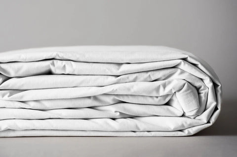 A neatly folded stack of the Cotton Duvet Cover Set by American Blossom Linens, highlighting its quality construction, rests against a plain, light gray background.