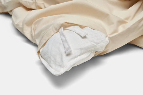 A close-up of the American Blossom Linens Cotton Duvet Cover Set, partially open to reveal a white duvet secured with fabric ties. The plain, well-lit background highlights the premium quality construction of these luxury bed linens.