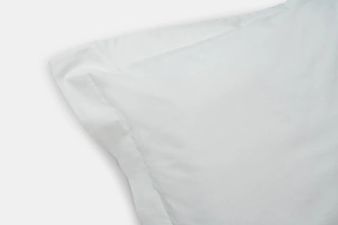 A close-up of two overlapping white pillows with crisp pillowcases showcases the quality construction of the Cotton Duvet Cover Set by American Blossom Linens against a light background, emphasizing premium bed linens.
