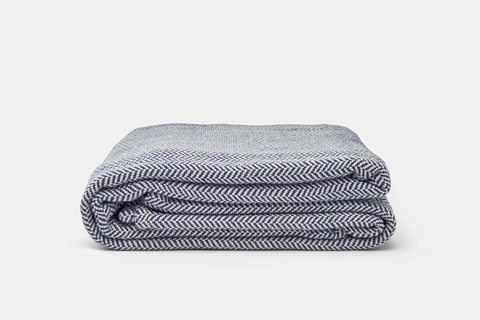 The Herringbone Weave Cotton Blanket from American Blossom Linens, shown neatly folded on a plain white background, adds a cozy, stylish layer to any space.