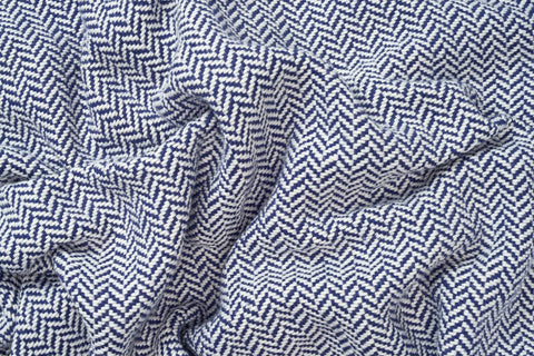 A close-up of the American Blossom Linens Herringbone Weave Cotton Blanket shows its crumpled blue and white chevron pattern, textured folds, and cozy, timeless appeal.