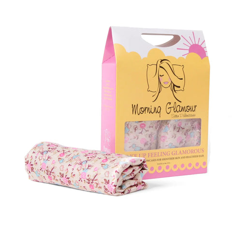 A folded satin pillowcase in a pink floral print sits next to its Morning Glamour box featuring a womans face and sun, highlighting these Standard/Queen silky pillowcases designed to reduce frizz. Set includes 2; available in multiple prints.
