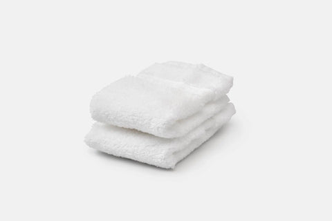 A neatly folded stack of three white, fluffy Bathroom Washcloths Made of Luxury USA Cotton by American Blossom Linens is displayed on a plain white background.