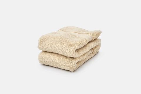 Two neatly folded, beige Bathroom Washcloths Made of Luxury USA Cotton by American Blossom Linens are stacked against a plain white background.