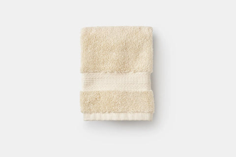 A beige Bathroom Washcloth made of luxury USA cotton by American Blossom Linens, featuring a textured band near one edge, is folded and set against a plain white background.