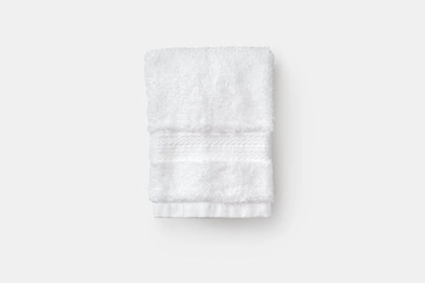 An American Blossom Linens Bathroom Washcloth made of luxury USA cotton, with a textured band at one end, is neatly folded and placed on a plain light gray surface.