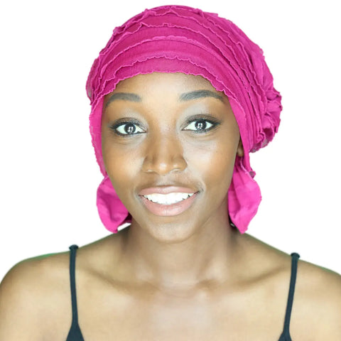 A smiling woman wearing the Chemo Beanies® Kathryn bright pink chemo scarf and a black spaghetti strap top looks directly at the camera against a white background.