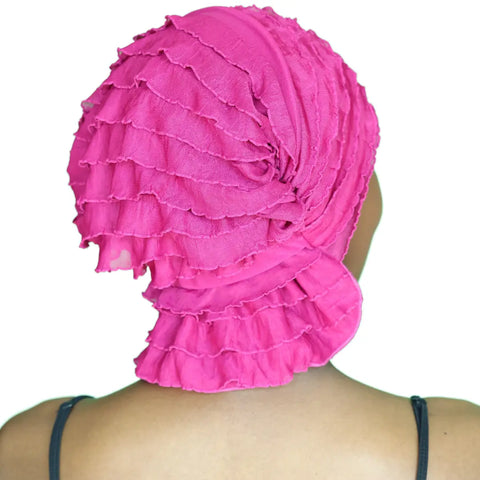 A person is seen from behind wearing the Chemo Beanies® Kathryn bright pink ruffled chemo head cover, with thin black shoulder straps, set against a plain white background.