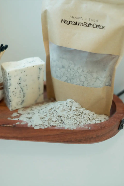 A wooden tray displays Shanti + Tula’s Magnesium Detox Bath Soak with Lavender & Bentonite Clay, along with a bar of soap and spilled magnesium-rich flakes—perfect for relaxation and sleep support. Made in the USA.