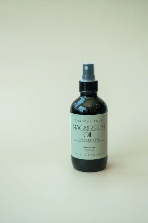 A dark Shanti + Tula Magnesium Oil Spray for Sleep, Stress & Muscle Recovery stands upright on a light surface. This pure, USA-made topical body oil is ideal for easing muscle soreness and promoting restful sleep.
