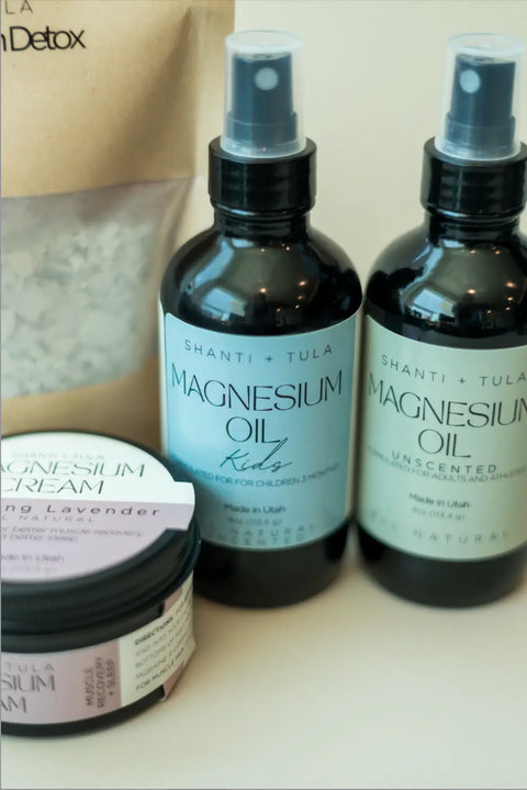 Two bottles of Shanti + Tula Magnesium Oil Spray for Sleep, Stress & Muscle Recovery, a jar of Magnesium Cream, and a Detox bag are arranged on a white surface—ideal for easing muscle soreness and supporting restful sleep.