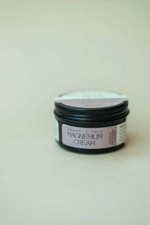 A black jar of Shanti + Tula Magnesium Recovery Cream for Sleep, Stress & Sore Muscles, with a lavender-infused light purple label, sits on a plain surface—highlighting hydrating, calming relief and support for muscle recovery. Made in the USA.