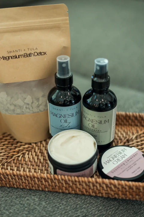 A woven tray displays an open jar of Shanti + Tula’s Magnesium Recovery Cream for Sleep, Stress & Sore Muscles—lavender-infused and hydrating—harnessing calming aromatherapy on a soft green surface.