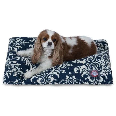 A brown and white Cavalier King Charles Spaniel is lying on the Majestic Pet French Quarter Rectangle Dog Bed in navy blue with a white floral pattern.