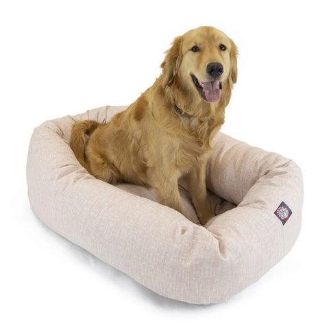 A golden retriever sits happily in the Majestic Pet Palette Heathered Bagel Dog Bed, a light beige, water resistant bed with excellent spine support, looking at the camera with its mouth open and tongue out.