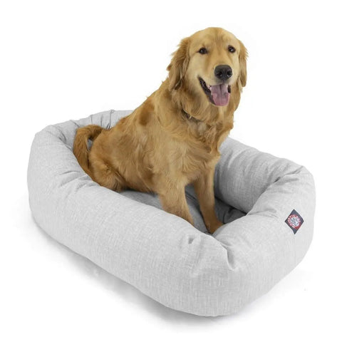 A golden retriever sits happily on the Majestic Pet Palette Heathered Bagel Dog Bed, a light gray rectangular bed with raised edges for spine support. The dog looks forward, mouth open and tongue out, enjoying this machine washable bed.