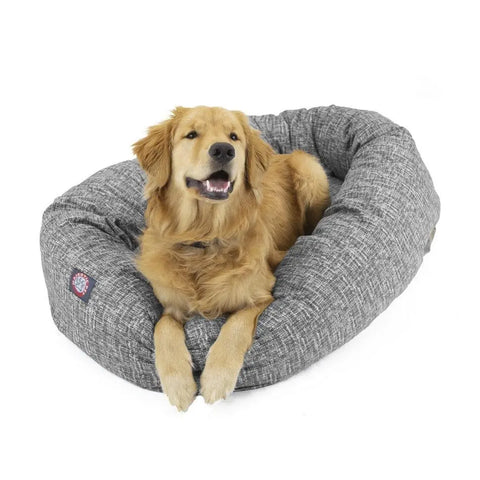 A golden retriever lounges in the Palette Heathered Bagel Dog Bed by Majestic Pet, an oval bed with water-resistant textured fabric and spine support, gazing up with a relaxed expression.