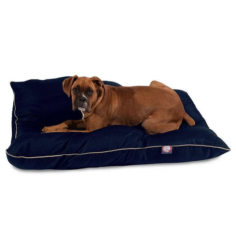A brown dog lies on a large, dark blue Majestic Pet Poly/Cotton Super Value Dog Bed with beige piping and a durable, machine-washable cover, looking at the camera against a plain white background.