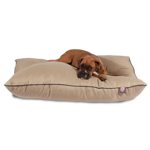 A brown dog lies on a large Majestic Pet Poly/Cotton Super Value Dog Bed with a beige, cushioned, machine-washable cover and black trim, looking toward the camera.