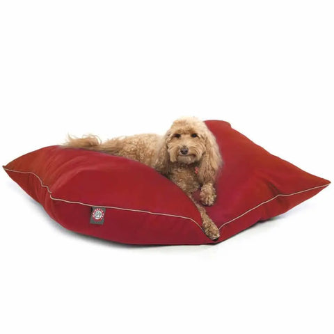 A fluffy, light brown dog lies on a large red Majestic Pet Poly/Cotton Super Value Dog Bed with white trim, a paw print logo on the front, and a fully machine washable cover for easy care.
