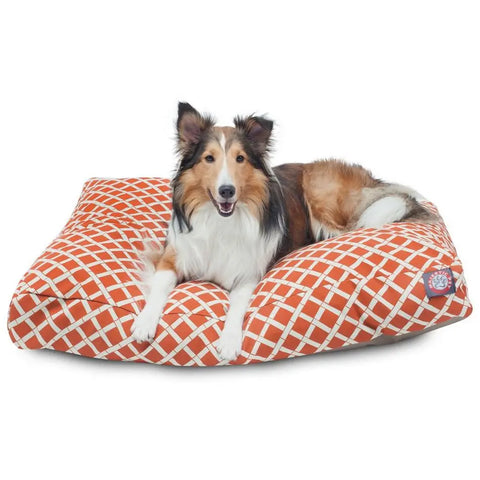 A fluffy collie lies on a Majestic Pet Bamboo Rectangle Dog Bed with an orange and white pattern, looking forward with its mouth slightly open.