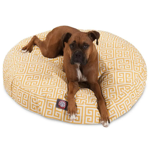 A brown dog with a white chest relaxes on the Majestic Pet Towers Round Dog Bed, which features a yellow-and-white Greek key pattern and a washable, removable cover—combining practicality and style as the dog stretches out.