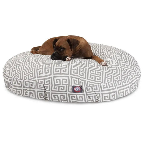 A brown dog rests on the Majestic Pet Towers Round Dog Bed, featuring a gray and white Greek key pattern and a removable, washable cover.