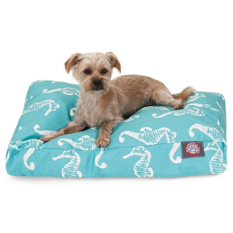 A small tan dog lies on the Majestic Pet Sea Horse Rectangle Dog Bed, featuring a turquoise cover with a white seahorse pattern, washable fabric, premium polyester fill, and a brand patch on the front corner.