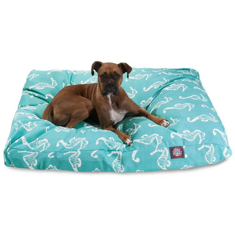 A brown dog lies on the Majestic Pet Sea Horse Rectangle Dog Bed, featuring a teal cover with white seahorses. The puffy bed has a removable cover for easy cleaning, and the dog is looking toward the camera.
