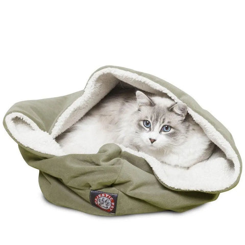 A fluffy white and gray cat with blue eyes is nestled inside a Majestic Pet Suede Burrow Cat Bed, featuring a soft Sherpa interior, paw print logo on the front, and plush white fleece lining for extra comfort.