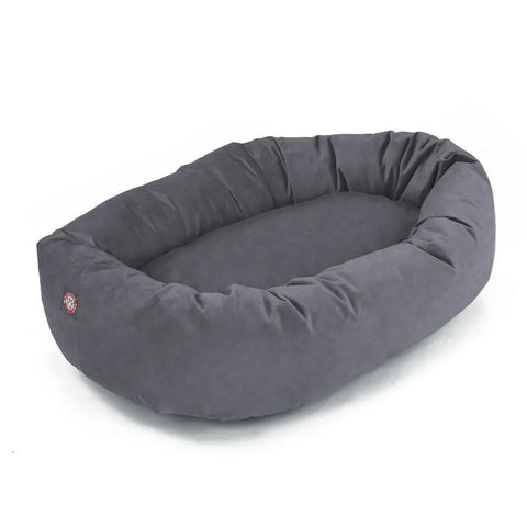 The Majestic Pet Suede Bagel Dog Bed is a large, oval bed with raised, cushioned sides and a soft polyester faux suede surface. A small round logo sewn onto one end adds a stylish touch.