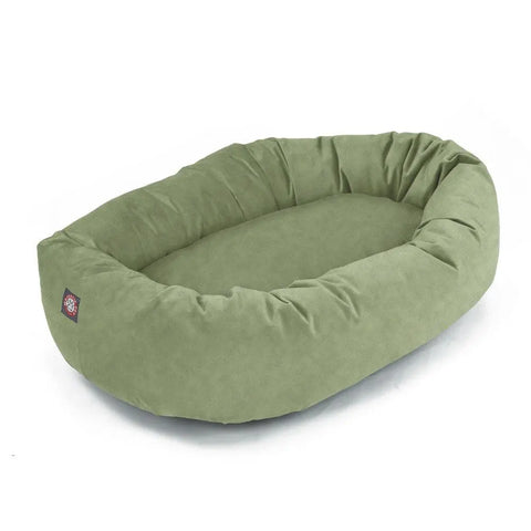 The Majestic Pet Suede Bagel Dog Bed is oval-shaped and green, made from durable polyester faux suede with raised cushioned sides, a soft flat base, a small paw print tag, and is machine washable for easy care.