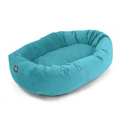 The Majestic Pet Velvet Bagel Dog Bed is a soft, oval bed in bright turquoise with a plush cushioned base, raised sides for comfort, and a small fabric tag—designed to provide extra spine support for your pet’s well-being.