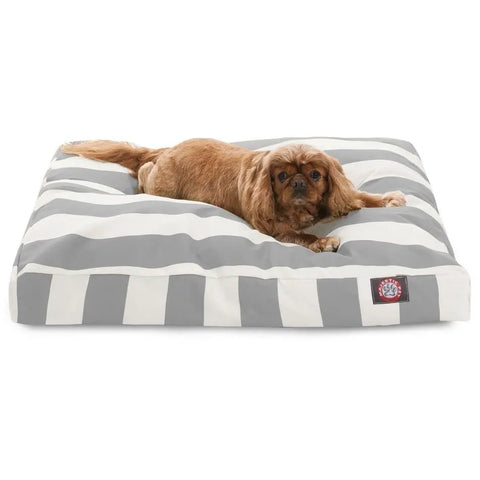 A small brown dog lies on the Majestic Pet Vertical Stripe Memory Foam Dog Bed, which is large, rectangular, with gray and white stripes and features a washable removable cover, looking toward the camera.