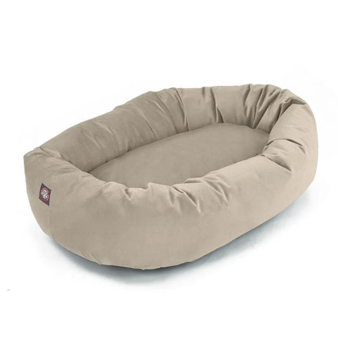 The Majestic Pet Poly/Cotton Bagel Dog Bed is beige and oval-shaped with raised cushioned sides, a soft sleeping surface, a small logo tag, and is machine washable for easy care.