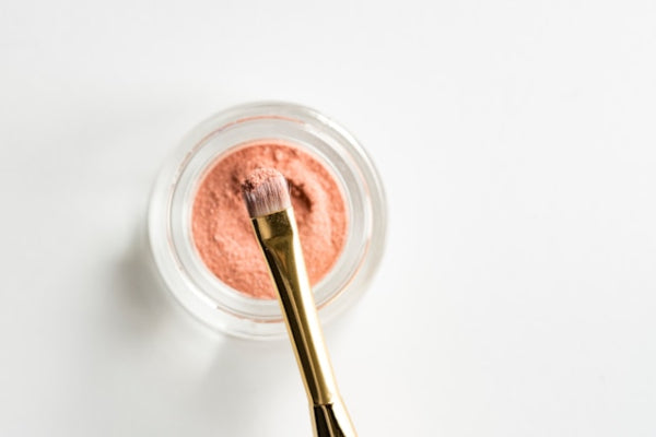 Pink cosmetic cream in a jar with a gold applicator on a white background