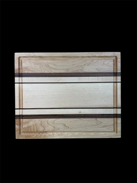 The B. James Design & Woodwork Maple and Zebra Wood Inlay Cutting Board With Juice Groove features striking light and dark wood grain patterns with two parallel dark stripes, set against a black background.