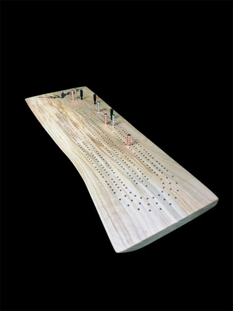The Maple Live Edge Cribbage Board With Mountain Engraving by B. James Design & Woodwork features a natural, curved edge and colored pegs in its scoring holes, displayed against a black background.