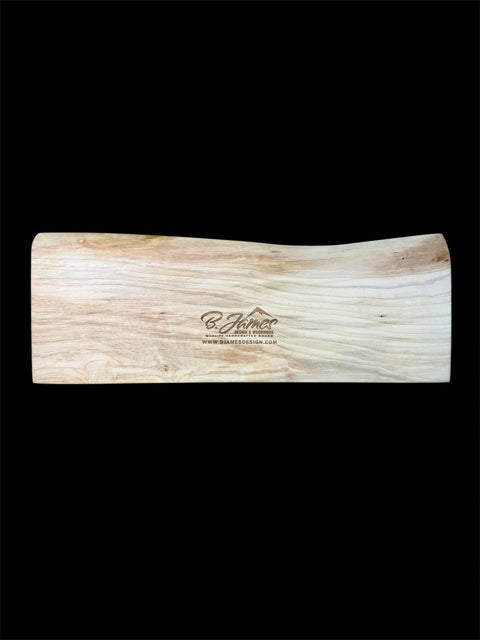 The Maple Live Edge Cribbage Board With Mountain Engraving by B. James Design & Woodwork features natural maple grain, a unique live edge, and a center-engraved logo and website, all set against a black background to highlight its craftsmanship.
