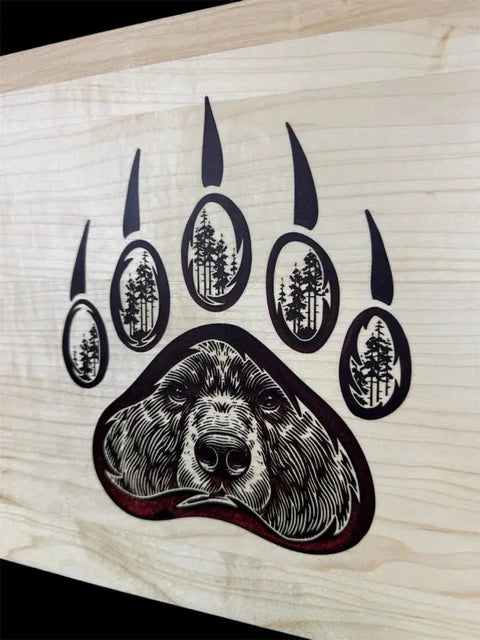 The Grizzly Inlay Serving Board by B. James Design & Woodwork features a handcrafted solid maple board with a stylized bear paw print, maroon epoxy inlaid toe pads, and detailed forest and bear motifs.
