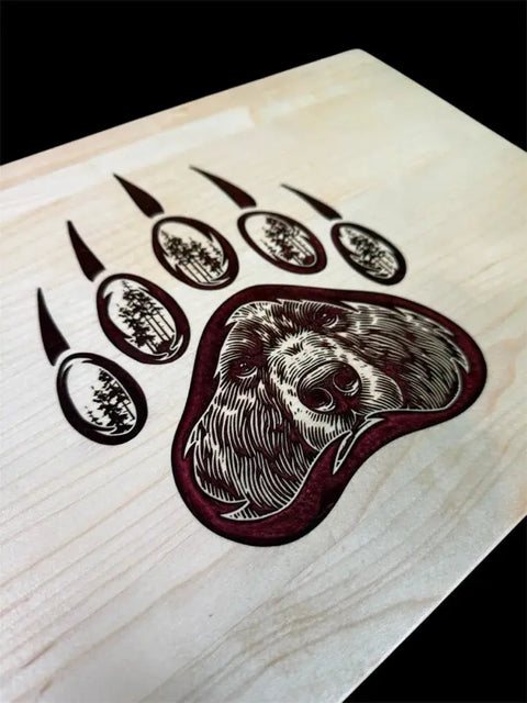 The Grizzly Inlay Serving Board by B. James Design & Woodwork features a handcrafted solid maple bear paw print with a detailed bear face in the pad, trees in each toe, and a maroon epoxy inlay for added uniqueness.