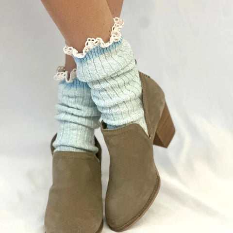 Close-up of a person wearing Catherine Coles MARLED Cotton Short Lace Boot Socks in Carolina Blue with taupe suede ankle boots, standing against a plain white background.