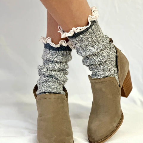 A person wears Catherine Cole MARLED Cotton Short Lace Boot Socks in grey, featuring a ruffled-knit texture and lace trim, paired with light brown heeled ankle boots on a plain white background.